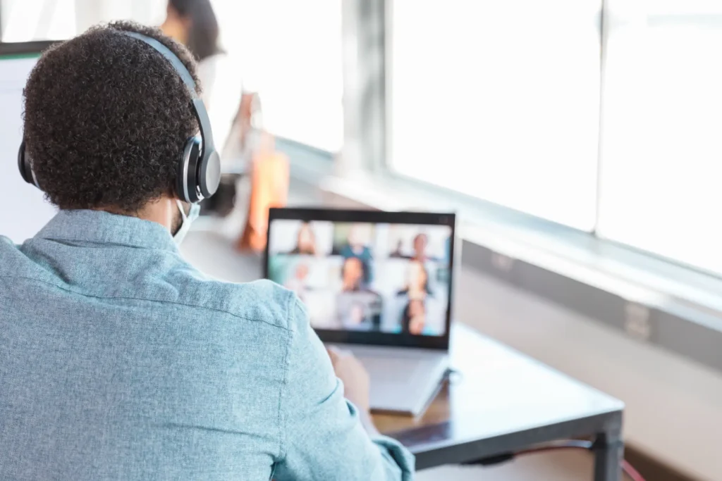 Reunião online em inglês: homem de fones acompanha a videochamada com vários participantes na tela