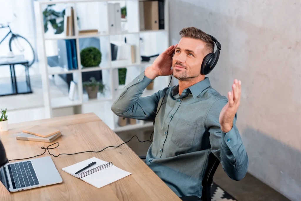 Profissional satisfeito ouvindo música em inglês com fones no escritório moderno